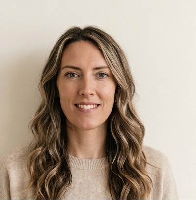 A smiling woman in her thirties with wavy blonde hair, bare skin